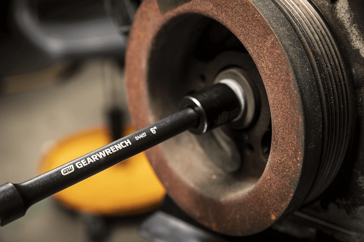 A GEARWRENCH 3/8" drive 6-inch impact extension bar (84407) connected to a socket, actively loosening a bolt on a rusty automotive pulley system.