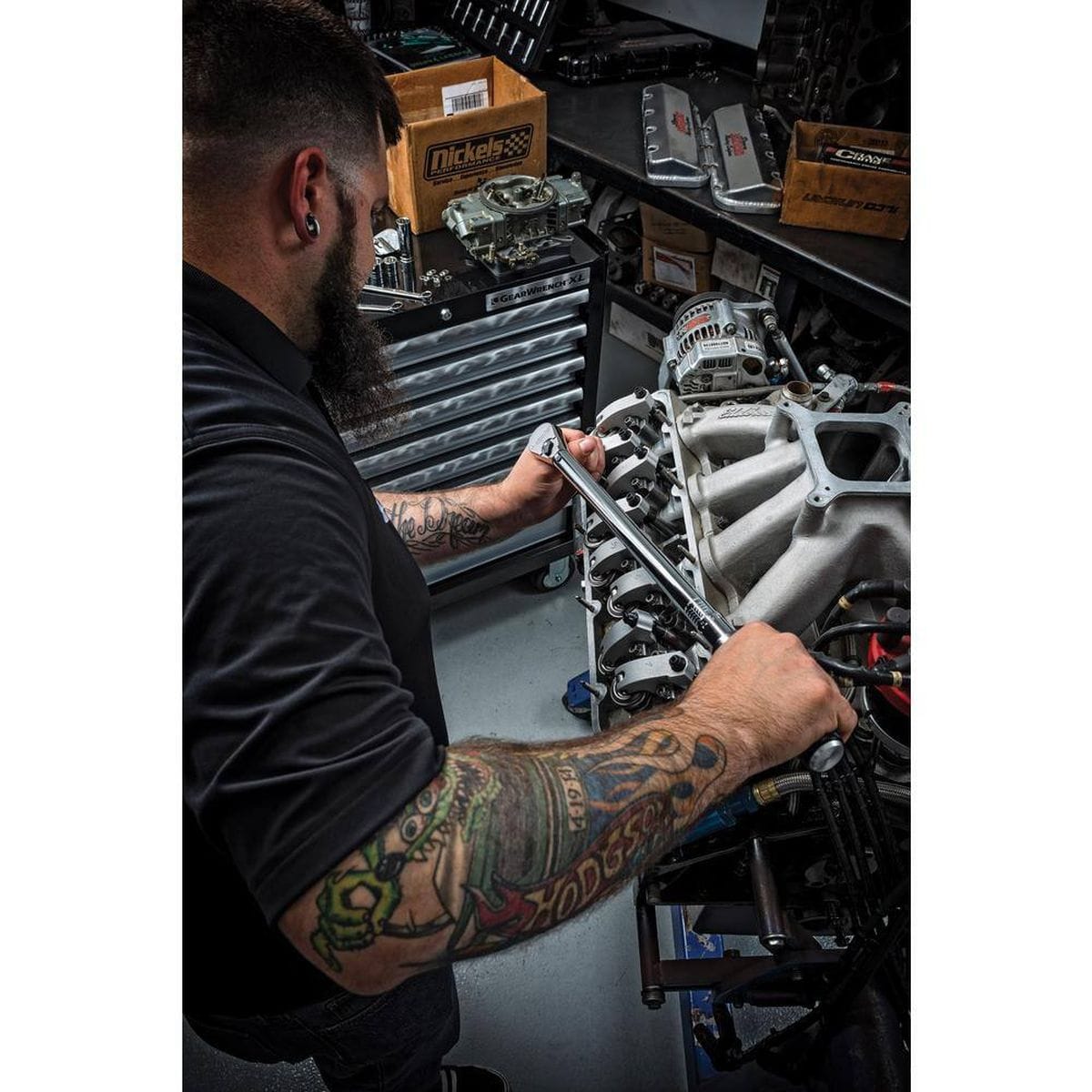 An application photo showing a professional mechanic with tattoos using the GEARWRENCH 85066M torque wrench to precisely tighten fasteners on a high-performance automotive engine in a shop environment.