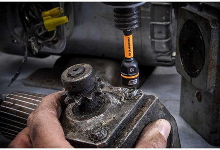 An action shot of the GEARWRENCH 86179 Bolt Biter being used with a cordless impact driver. A technician is shown extracting a damaged, greasy bolt from an industrial machine, demonstrating the tool's effectiveness in real-world maintenance settings.
