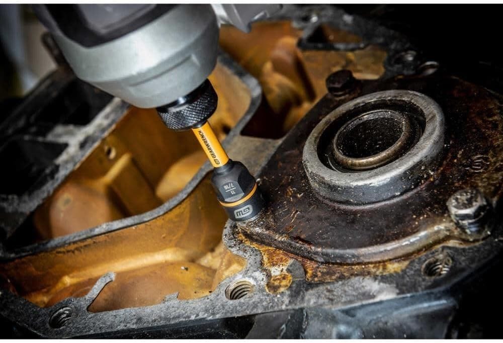 Action photograph showing the Bolt Biter nut driver extracting a rusted fastener from an automotive engine block. The image highlights the 1/4-inch hex shank connected to a cordless impact tool, emphasizing the device's durability in greasy, high-torque environments.