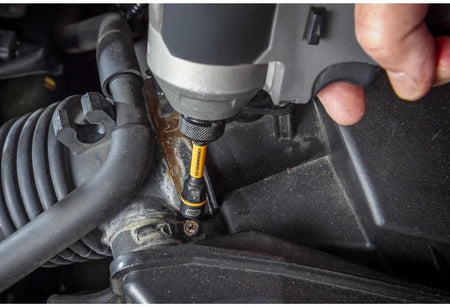 Action shot featuring the GEARWRENCH 3/8-inch nut extractor removing a corroded bolt from a vehicle's air intake housing. The photograph demonstrates the tool's slim profile and tapered entry, allowing access to damaged fasteners in tight engine compartments.