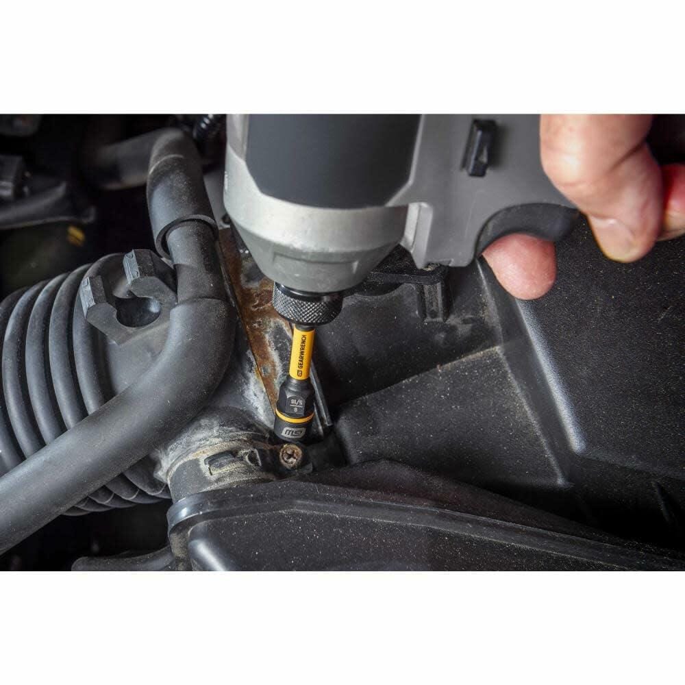 A person uses an impact driver with a GEARWRENCH Bolt Biter nut extractor to remove a bolt from a rusty bracket in a car's engine bay.