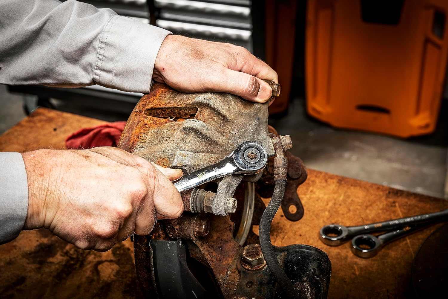 An action shot of a technician using a ratcheting wrench with a GEARWRENCH Bolt Biter insert to remove a severely corroded bleeder valve on an automotive brake caliper assembly.