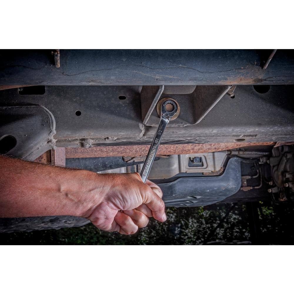 An action shot from beneath a vehicle showing a technician using the GEARWRENCH 1/2 inch combination wrench to access a chassis bolt, demonstrating the tool's durability in rugged automotive environments.