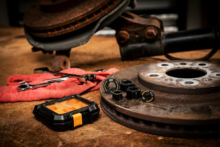 The 5-piece Bolt Biter insert set and its case displayed on a workbench next to a rusty brake rotor and other tools.