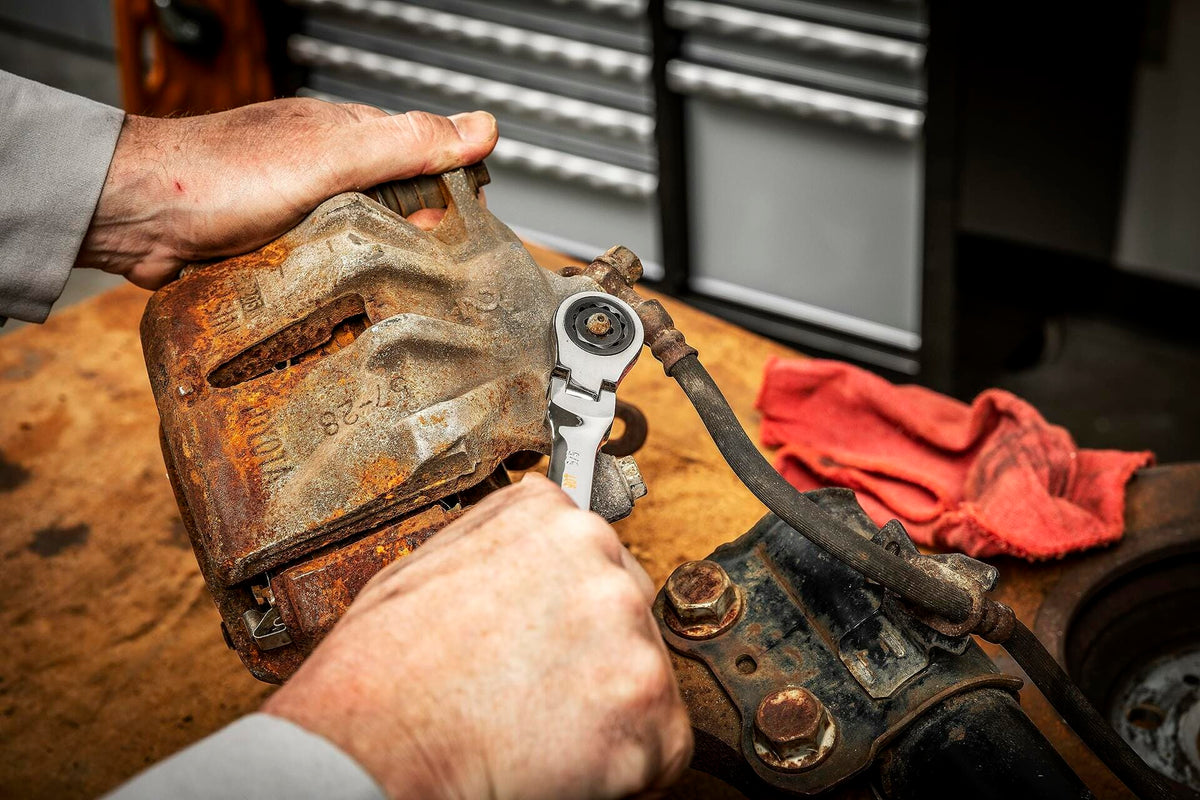 A mechanic uses a GEARWRENCH Bolt Biter insert and a ratcheting wrench on a rounded bolt on a rusty automotive brake caliper.