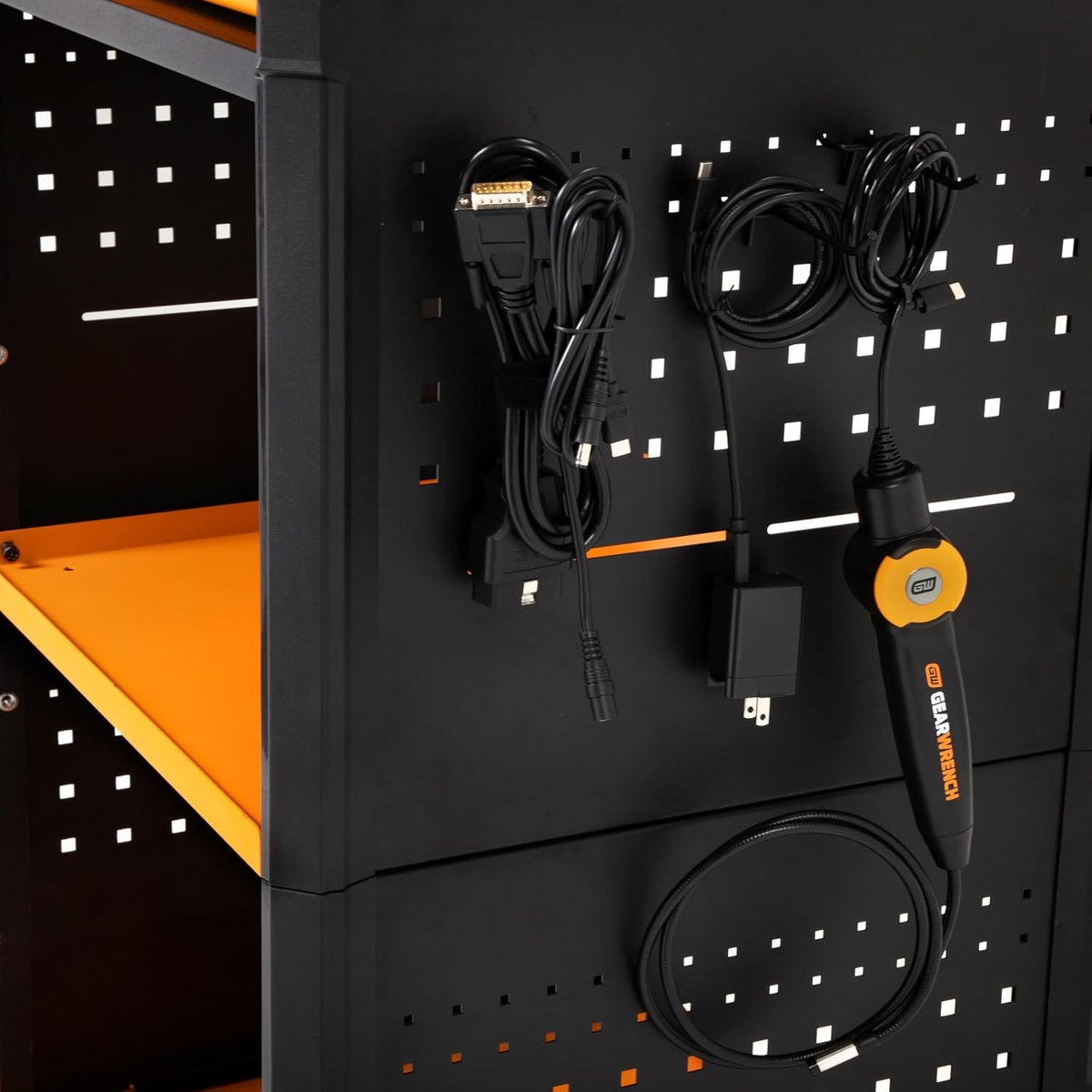 A close-up view of the side peghole organizer plate showing hung diagnostic interface items including a bundled black OBD2 cable harness, charger block wires, and a matching orange-trimmed electronic inspection bore probe.