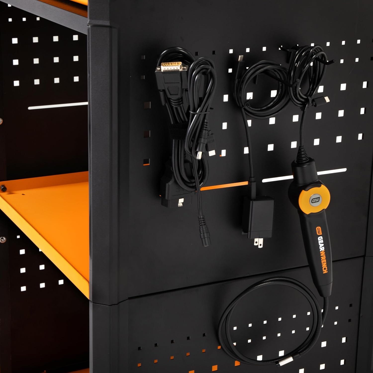 A close-up view of the side peghole organizer plate showing hung diagnostic interface items including a bundled black OBD2 cable harness, charger block wires, and a matching orange-trimmed electronic inspection bore probe.