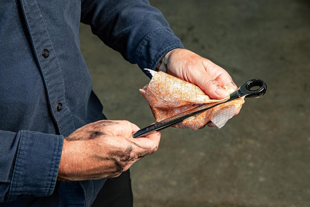 A mechanic cleans automotive oil and grease off a chrome combination wrench using a highly absorbent, pre-moistened industrial shop towel.
