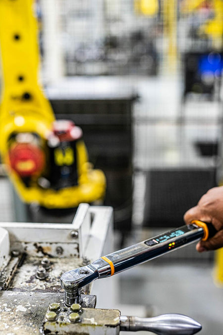 A worker applying torque with the GEARWRENCH electronic wrench on a machine, with the digital display showing the real-time measurement and indicator lights flashing.