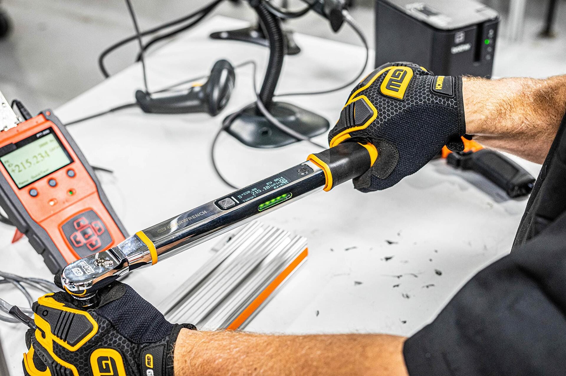 A worker wearing gloves calibrating or testing the electronic torque wrench against a digital readout device on a workbench.