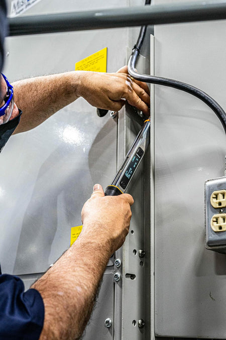 A worker using the GEARWRENCH electronic torque wrench to tighten a fastener in a tight spot on industrial machinery.