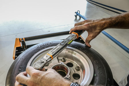 A mechanic using the GEARWRENCH electronic torque wrench to tighten lug nuts on a tire assembly, viewing the digital display for accurate torque readings.