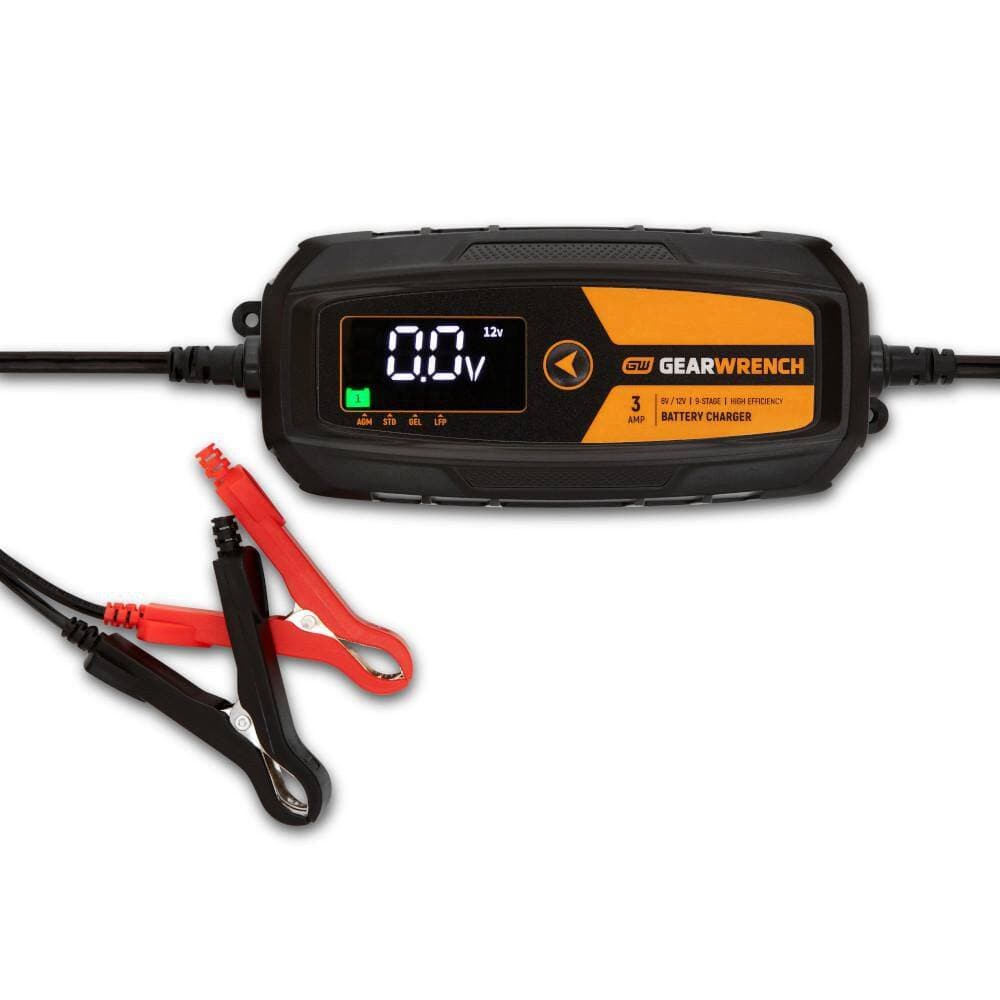 A studio product view of the GEARWRENCH GWBC030 3A battery charger and maintainer. The image features the central digital control unit in black and molten orange, accompanied by professional-grade red and black battery terminal clamps.