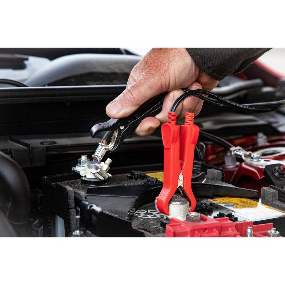 A close-up action shot showing a technician's hand securing the heavy-duty red and black terminal clamps to an automotive battery. The image highlights the secure grip and low-profile design of the clamps, ensuring a reliable connection for the 9-stage intelligent charging cycle.