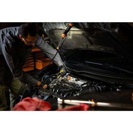 Action shot of a mechanic using the GEARWRENCH flex head light attached to a vehicle hood, directing light deep into the engine bay for a detailed maintenance inspection.