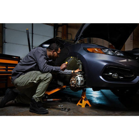 A technician using the GEARWRENCH GWFL105 rechargeable light to illuminate the wheel well and suspension components of a car while it is supported by a jack stand.
