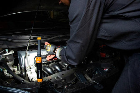 A professional technician using the magnetic base of the GEARWRENCH work light to attach it to a car hood while performing an engine inspection and oil level check.