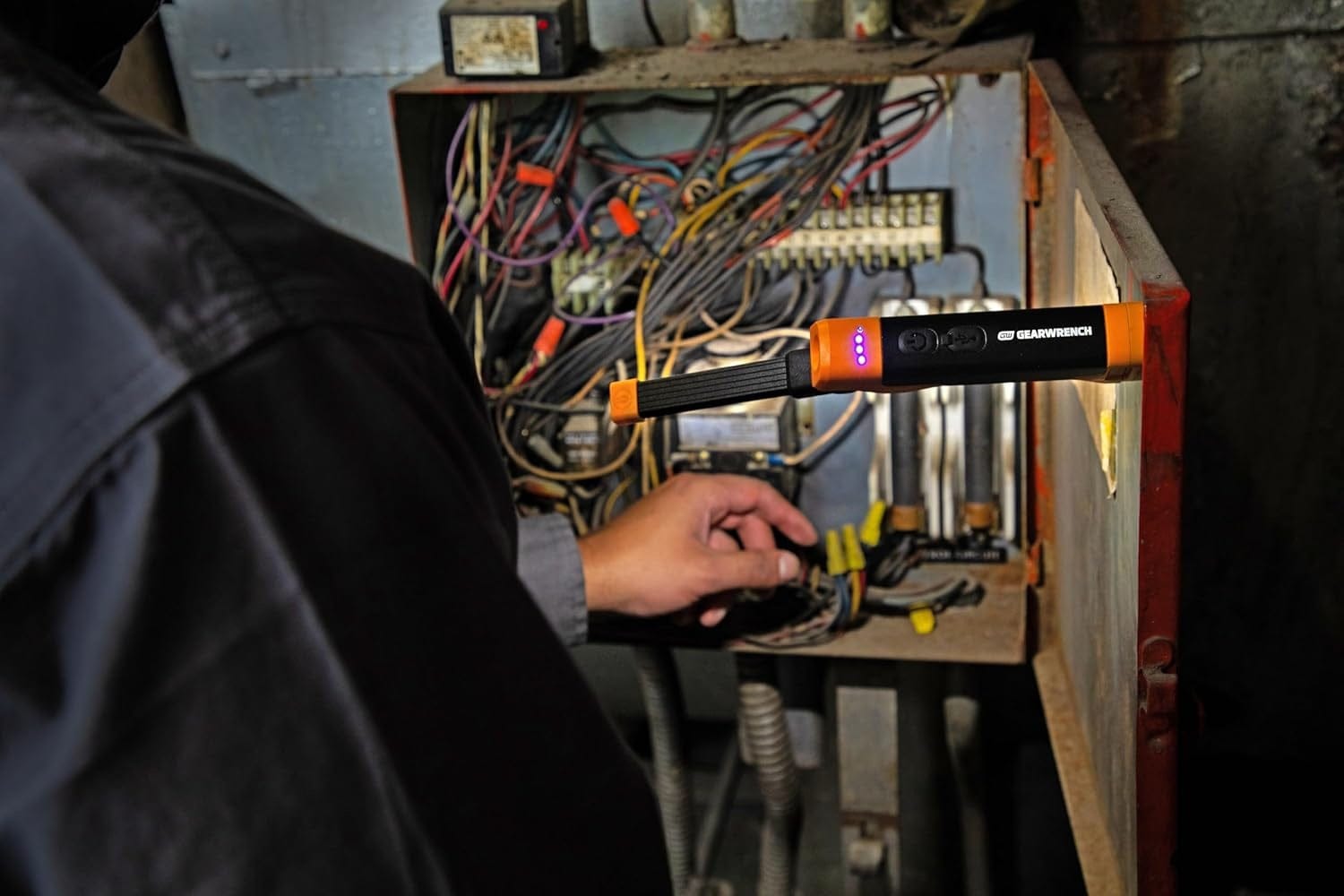 A professional using the GEARWRENCH rechargeable flex head light to illuminate an electrical panel, showcasing the magnetic base mounted to the metal door for hands-free industrial inspection.