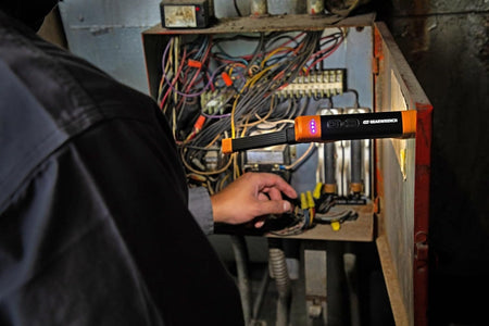 A professional using the GEARWRENCH rechargeable flex head light to illuminate an electrical panel, showcasing the magnetic base mounted to the metal door for hands-free industrial inspection.