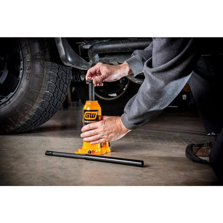 Professional application shot showing a technician positioning the GEARWRENCH 6-ton hydraulic bottle jack under the frame of a vehicle on a concrete floor.