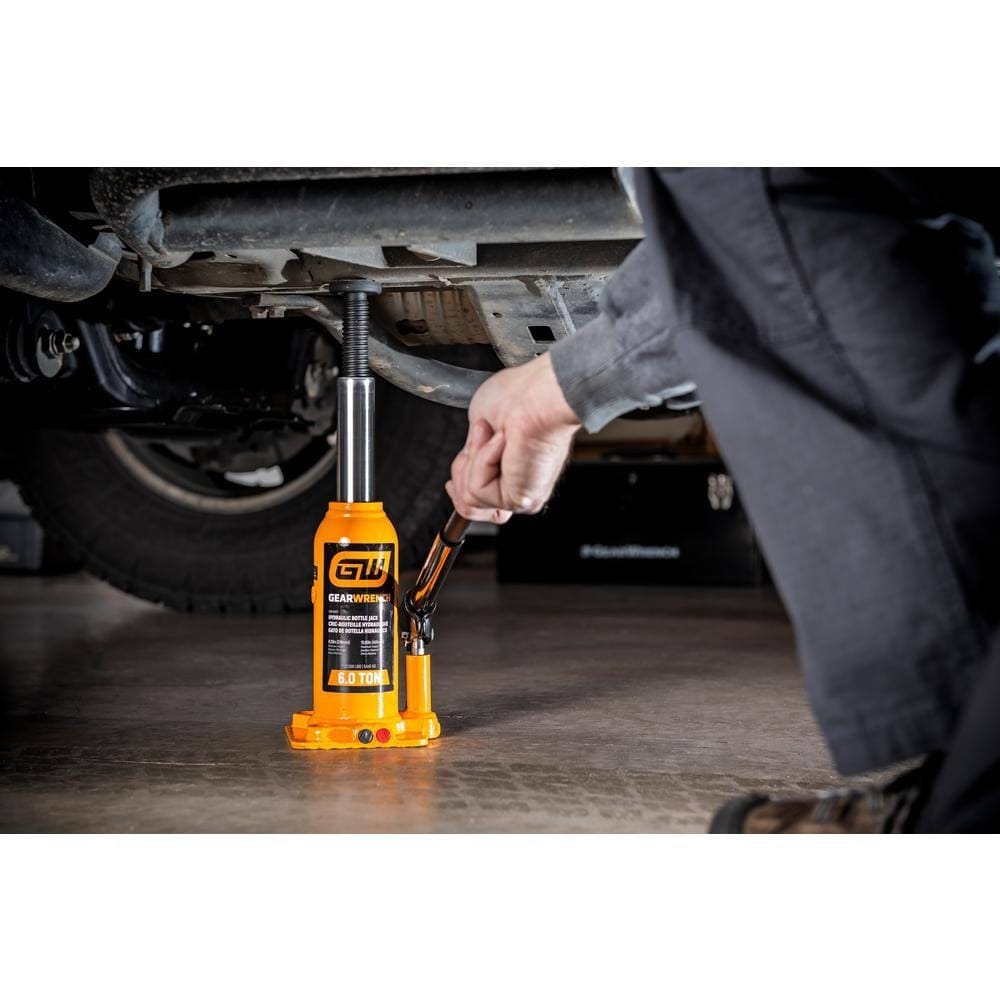 A tradesperson using the GEARWRENCH GWHBJ6T bottle jack to lift a vehicle, demonstrating the manual pump operation and the stability provided by the wide base and high-grip saddle.