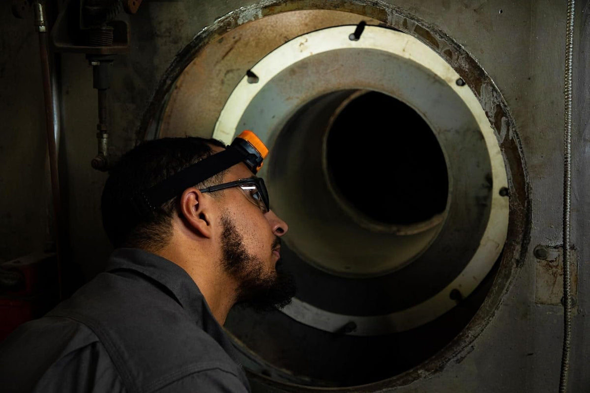 A technician wearing the illuminated GEARWRENCH headlamp inspects the dark interior of a large industrial pipe.