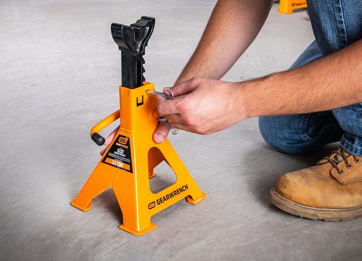 Close-up of a person's hands engaging the double lock pin on a GEARWRENCH GWJS3T jack stand, illustrating the added layer of protection and manual safety locking mechanism.
