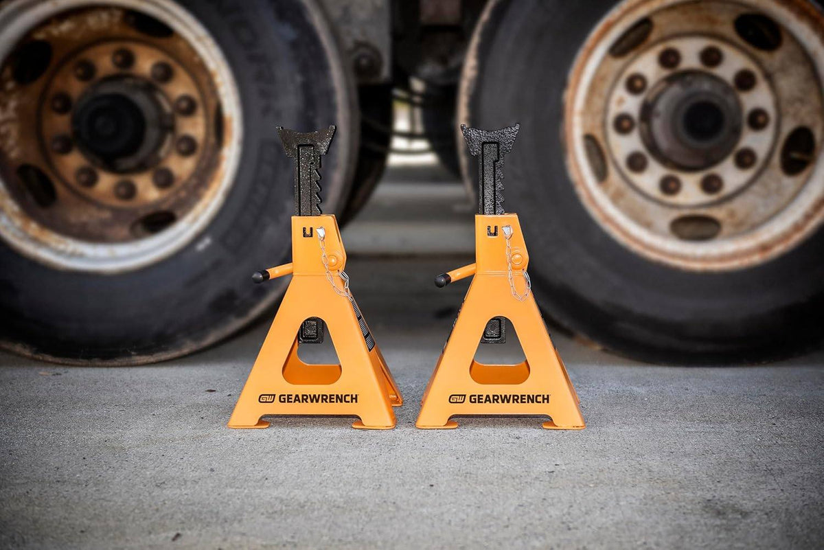 A pair of 6 ton GEARWRENCH jack stands positioned on a concrete shop floor in front of heavy-duty truck tires to demonstrate professional industrial application and stability.