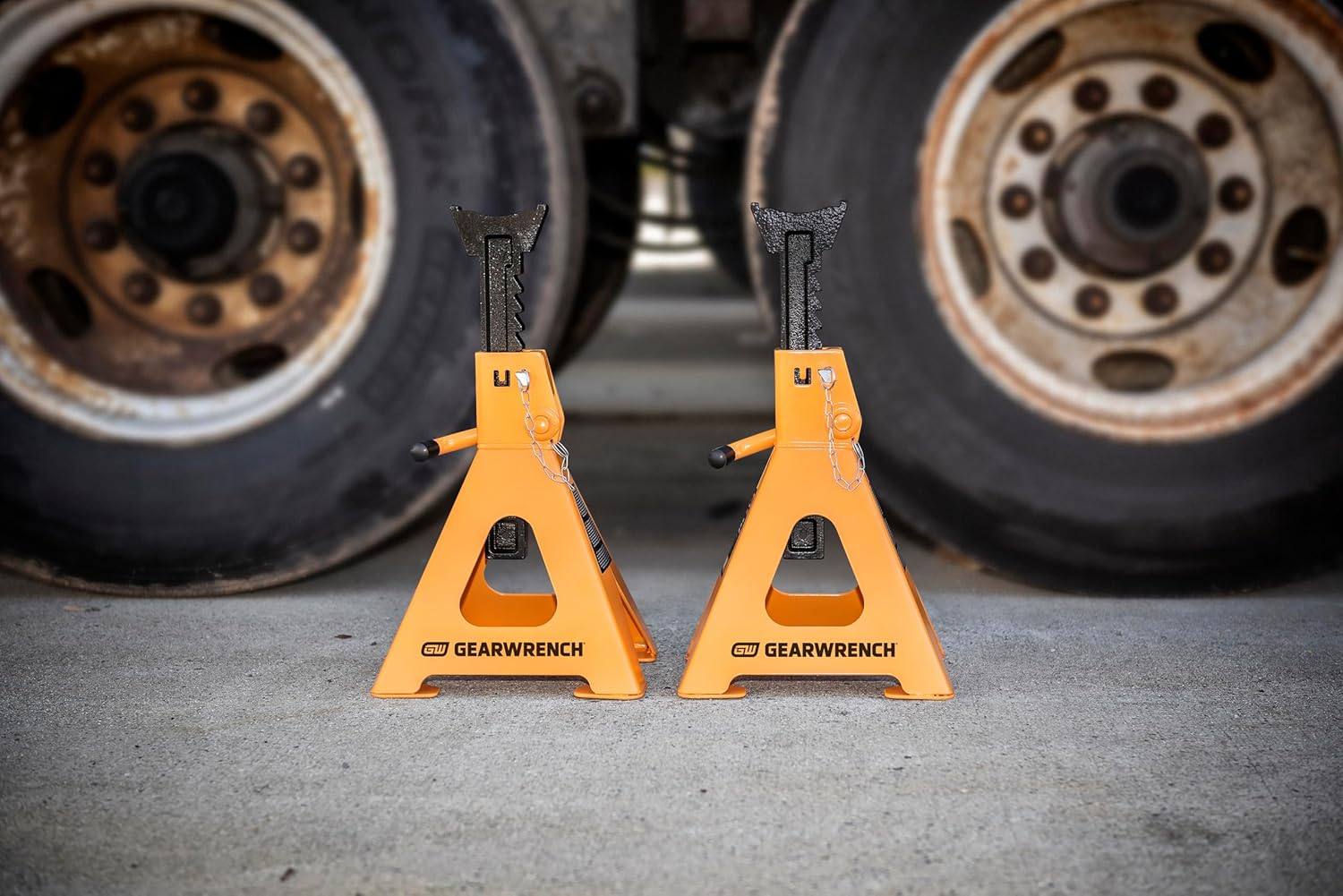 A pair of 6 ton GEARWRENCH jack stands positioned on a concrete shop floor in front of heavy-duty truck tires to demonstrate professional industrial application and stability.