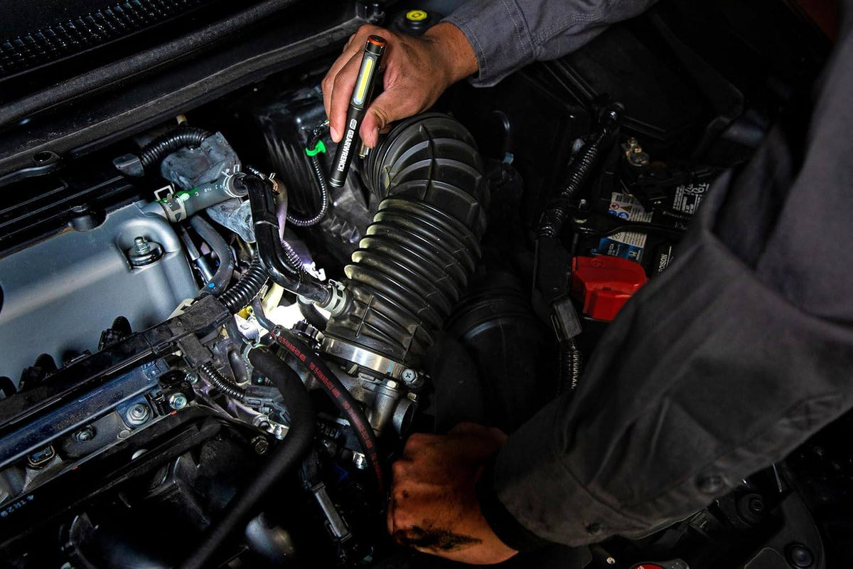 An action shot of the GEARWRENCH GWPL pen light being used to inspect a vehicle engine bay, with the magnetic clip attached to the underside of the hood for hands-free professional illumination.