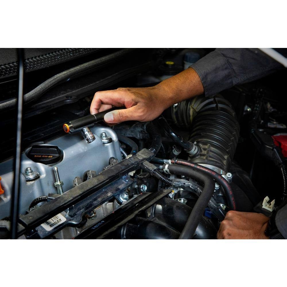 An action shot of the GEARWRENCH GWPL pen light being used to inspect a vehicle engine bay, with the magnetic clip attached to the underside of the hood for hands-free professional illumination.