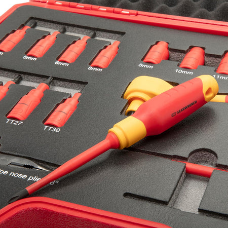 A macro close-up view of a red and yellow GEARWRENCH insulated flat head screwdriver sitting on top of the dark grey shadow foam tray insert, showing the clean molded insulation layer and the labeled socket trays inside the red carrying case.
