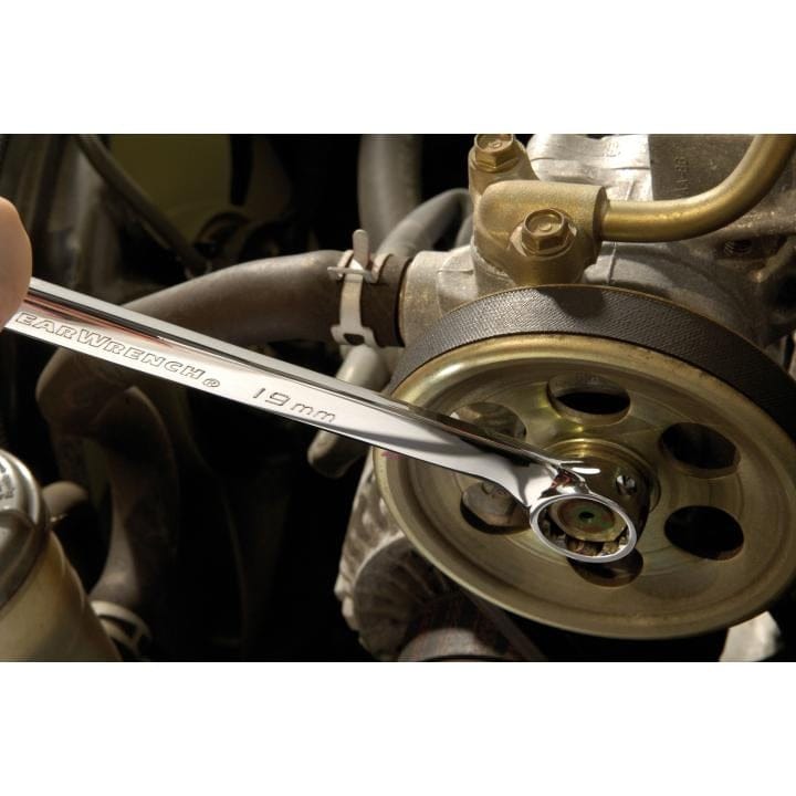 A close-up action shot of a GearWrench 19mm combination wrench being used on a bolt on an engine's accessory pulley.