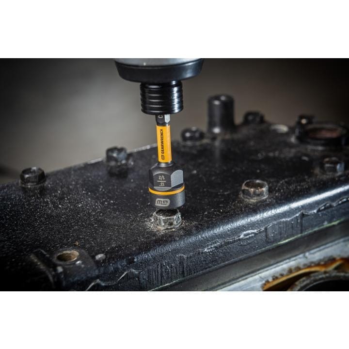 Close-up of GearWrench socket tool engaging a large bolt on a metal engine component, showing 2 1/4 inch and 57 mm size markings for heavy-duty mechanical applications.