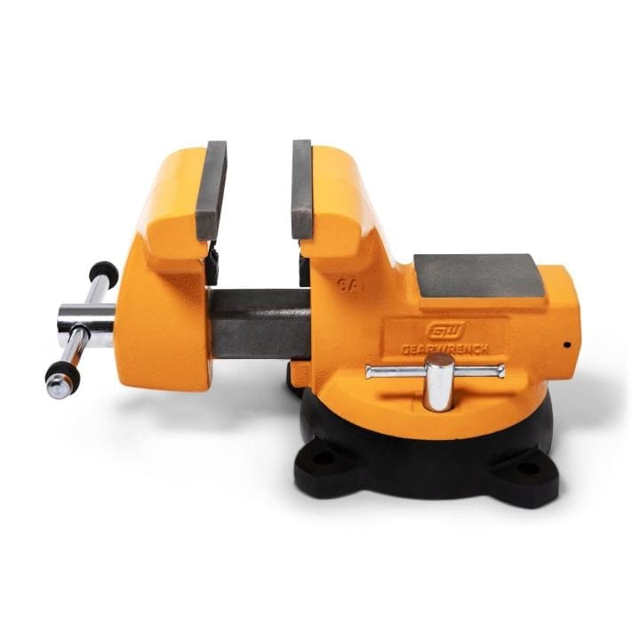Orange and black GearWrench bench vise mounted on a circular base with four mounting holes, showing textured jaws and adjustment handle.
