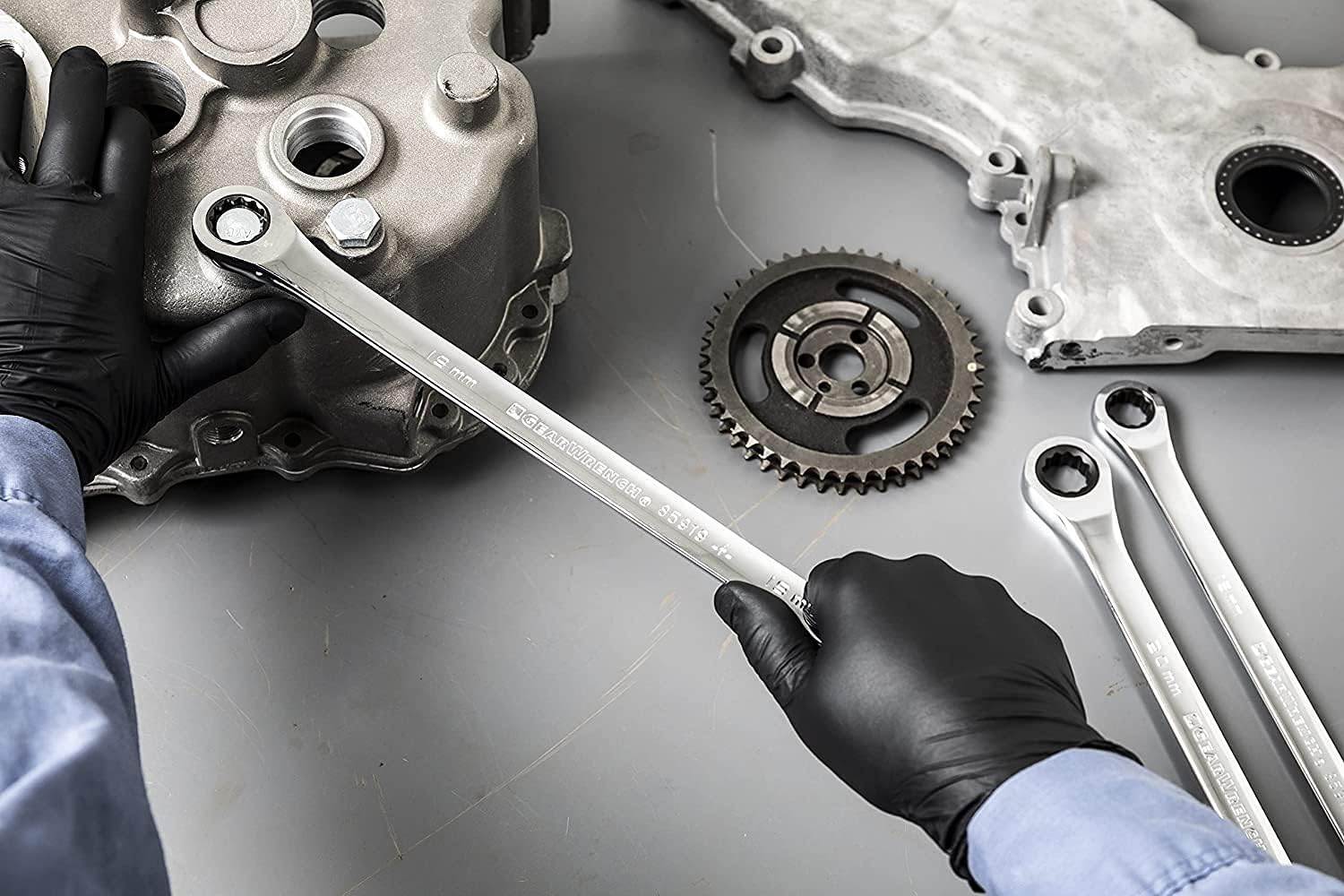 Mechanic hands using a GearWrench XL GearBox ratcheting wrench to tighten a bolt on a metal engine casing.