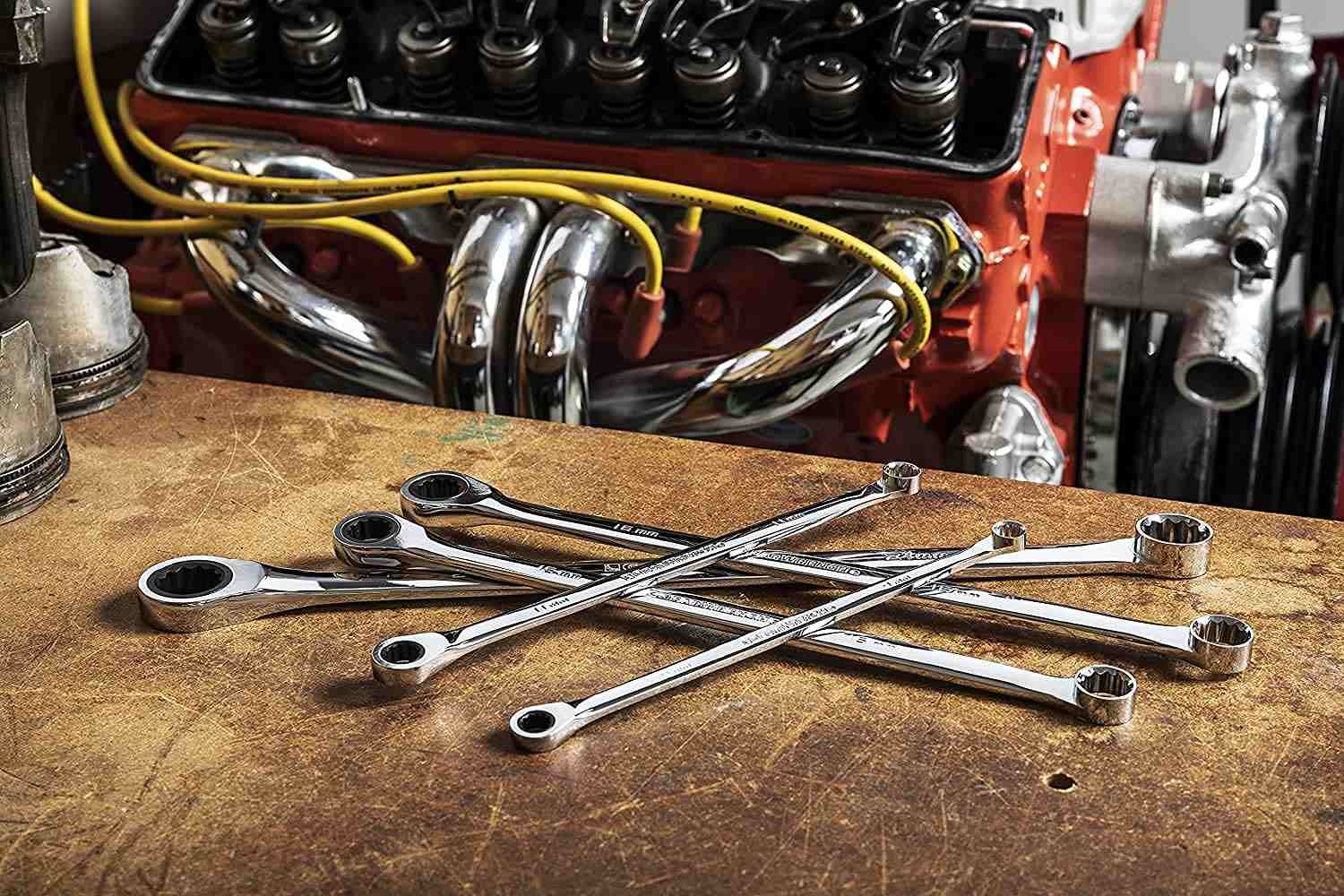 A selection of GearWrench XL GearBox double box ratcheting wrenches scattered on a wooden workbench in front of an engine block.