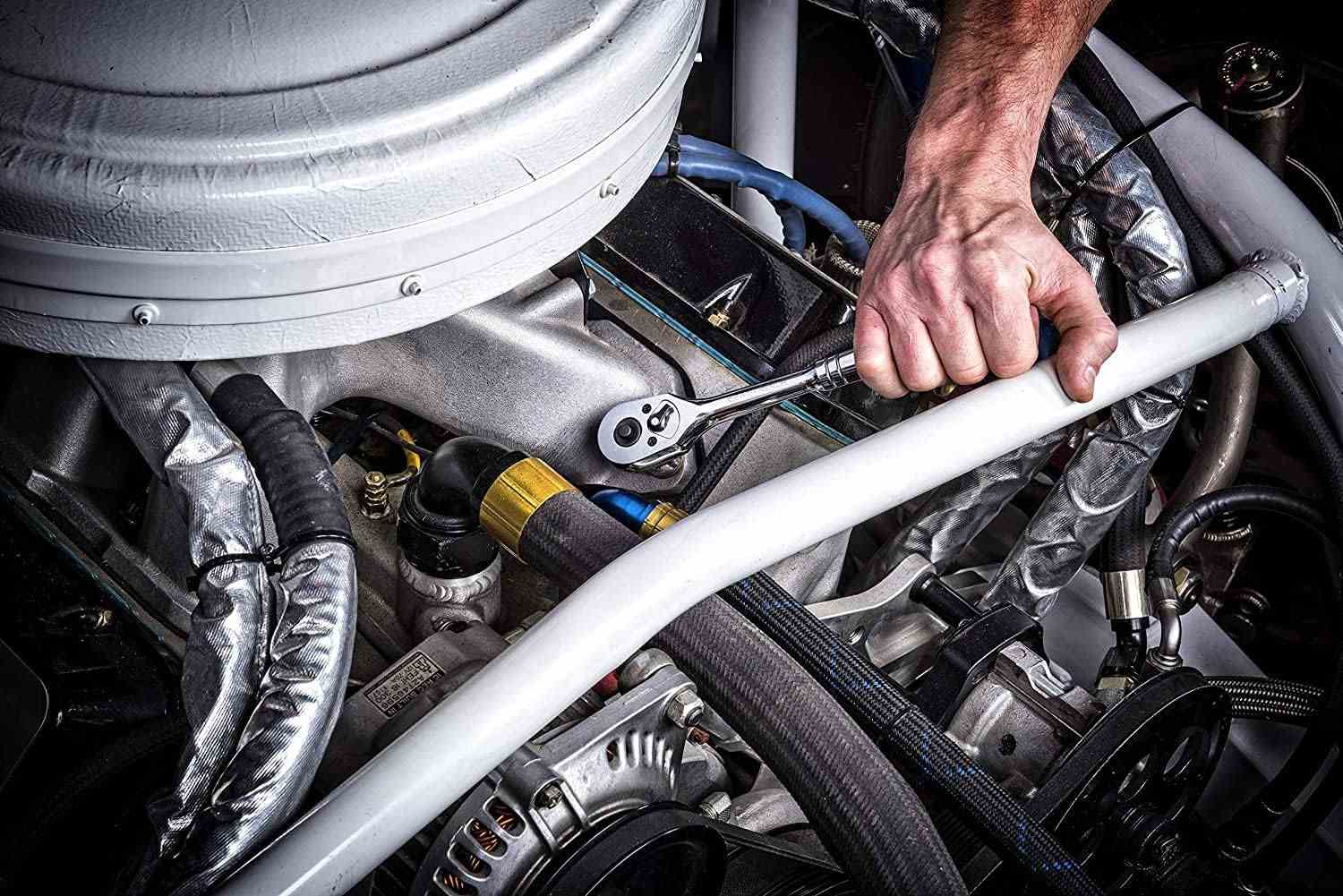 A close-up action shot of a hand using a GEARWRENCH 90-tooth ratchet in the tight confines of a race car engine bay.