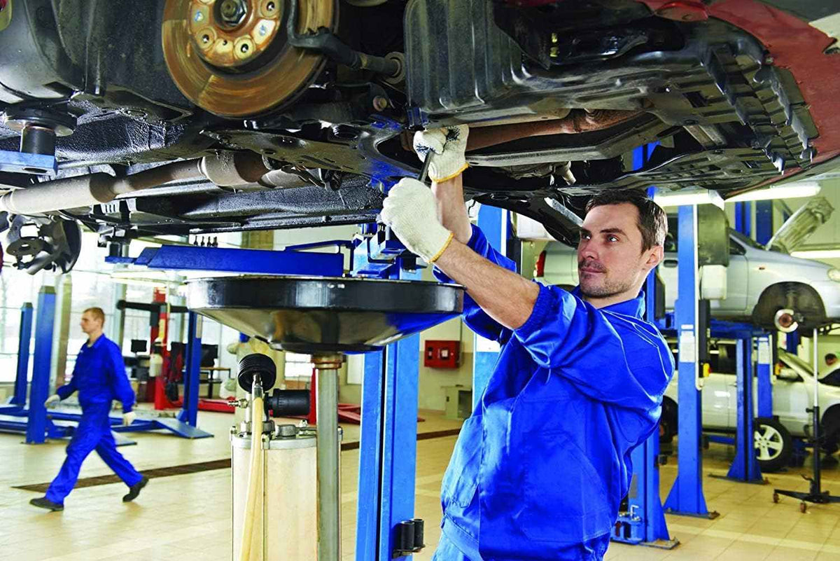 A mechanic in blue coveralls works under a car on a lift, using a wrench from the tool set.