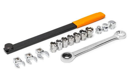 Complete 15-piece serpentine belt tool set displayed, featuring a long black extension bar with an orange handle, a chrome ratcheting wrench, three crowfoot wrenches, three drive adapters, and seven sockets.