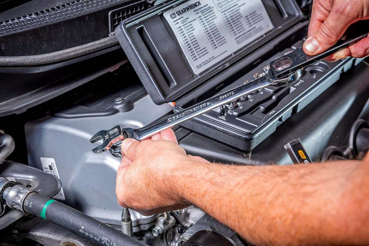 Close-up action shot of a mechanic's hands connecting the long extension bar to the ratcheting wrench to create a leverage tool for a belt tensioner.