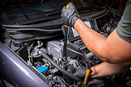 Action shot of a mechanic using the assembled serpentine belt tool with the long orange handle to compress a tensioner deep inside a vehicle engine compartment.