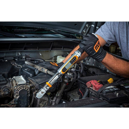Person using a digital torque wrench on a car engine; wearing black gloves and gray shirt in an engine bay with visible components.