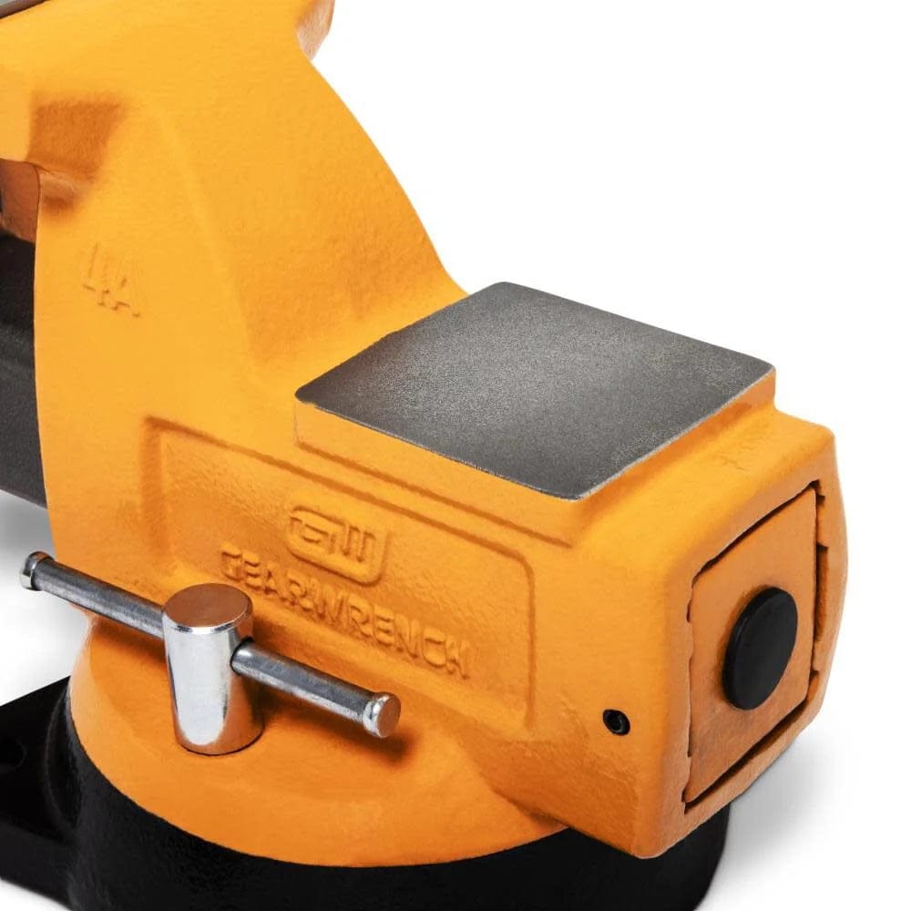 Detailed view of a orange GearWrench bench vise with embossed branding, flat anvil surface, rotating base, and large adjustment knob in a workshop environment.