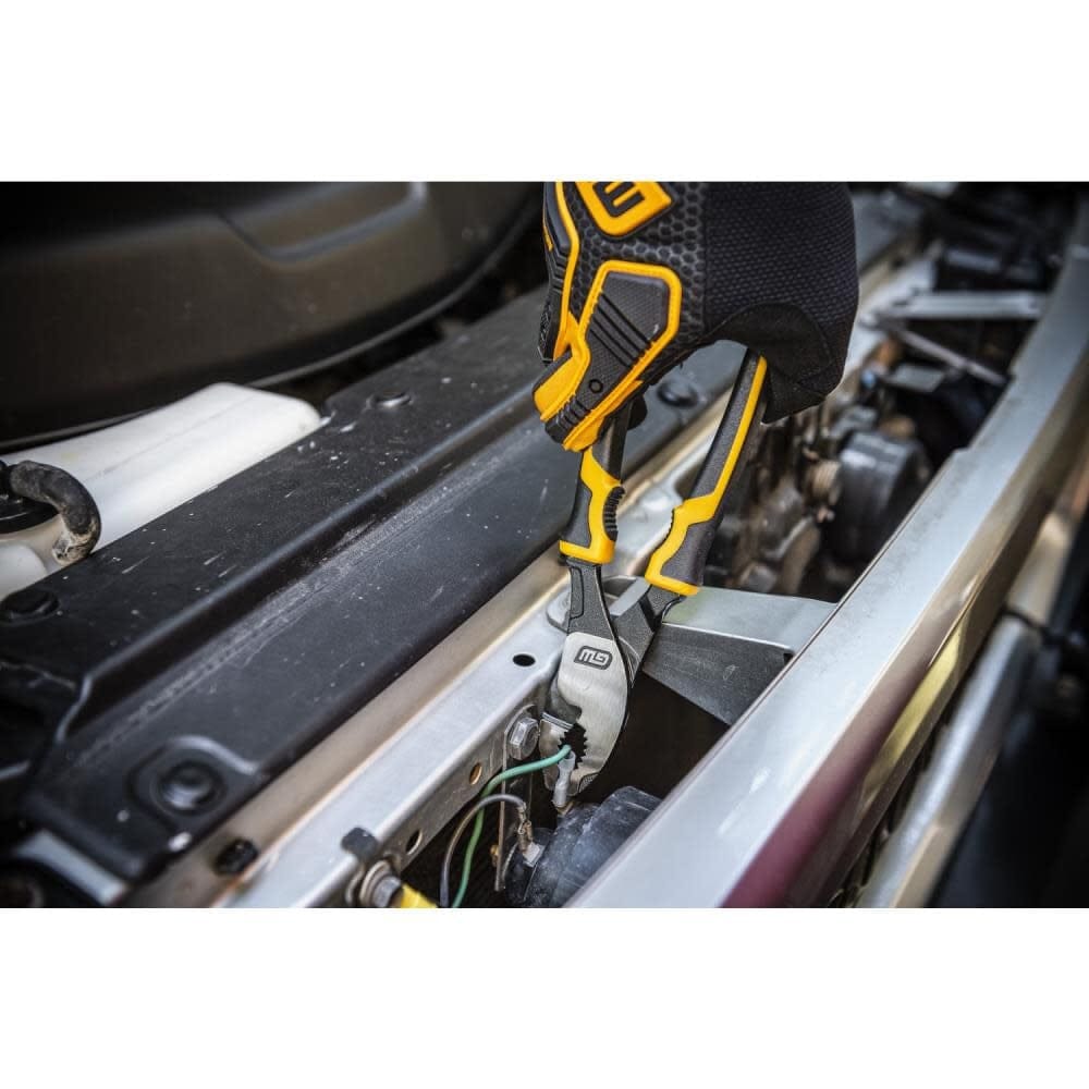 Close-up of a gloved hand using GearWrench pliers to grip a wire inside a vehicle engine compartment; various metal and electrical components are visible.
