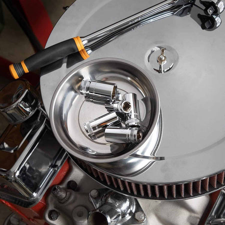 High-angle shot of loose chrome sockets sitting in a stainless steel magnetic parts tray resting on a classic car engine air cleaner.