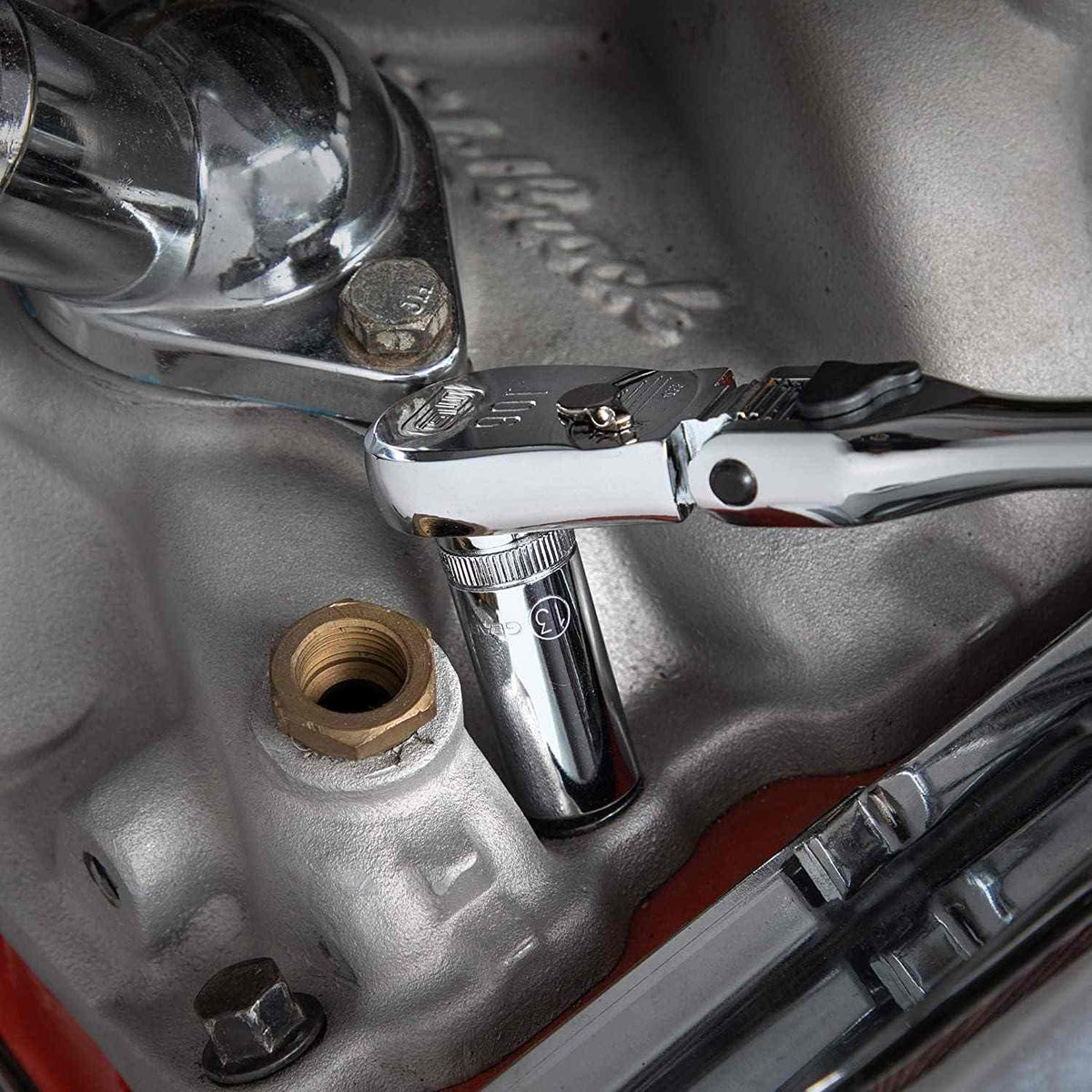 Action shot of a ratchet and socket with an extension bar tightening a bolt on a silver engine component.