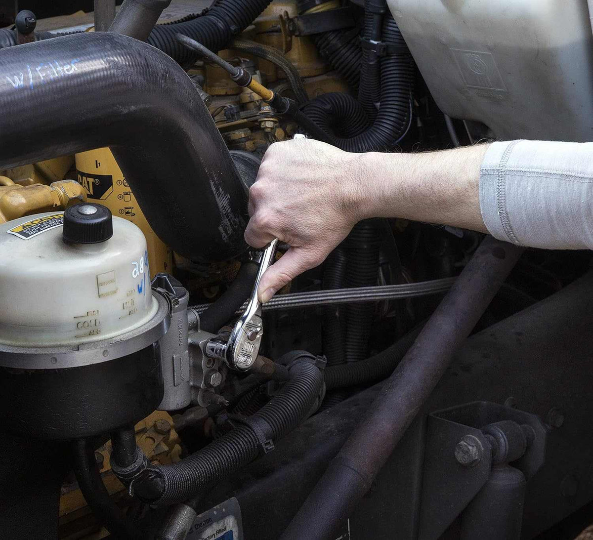 Action shot showing a professional mechanic using a GearWrench 90-tooth ratchet from the 80550 set to perform engine maintenance in a tight vehicle compartment.