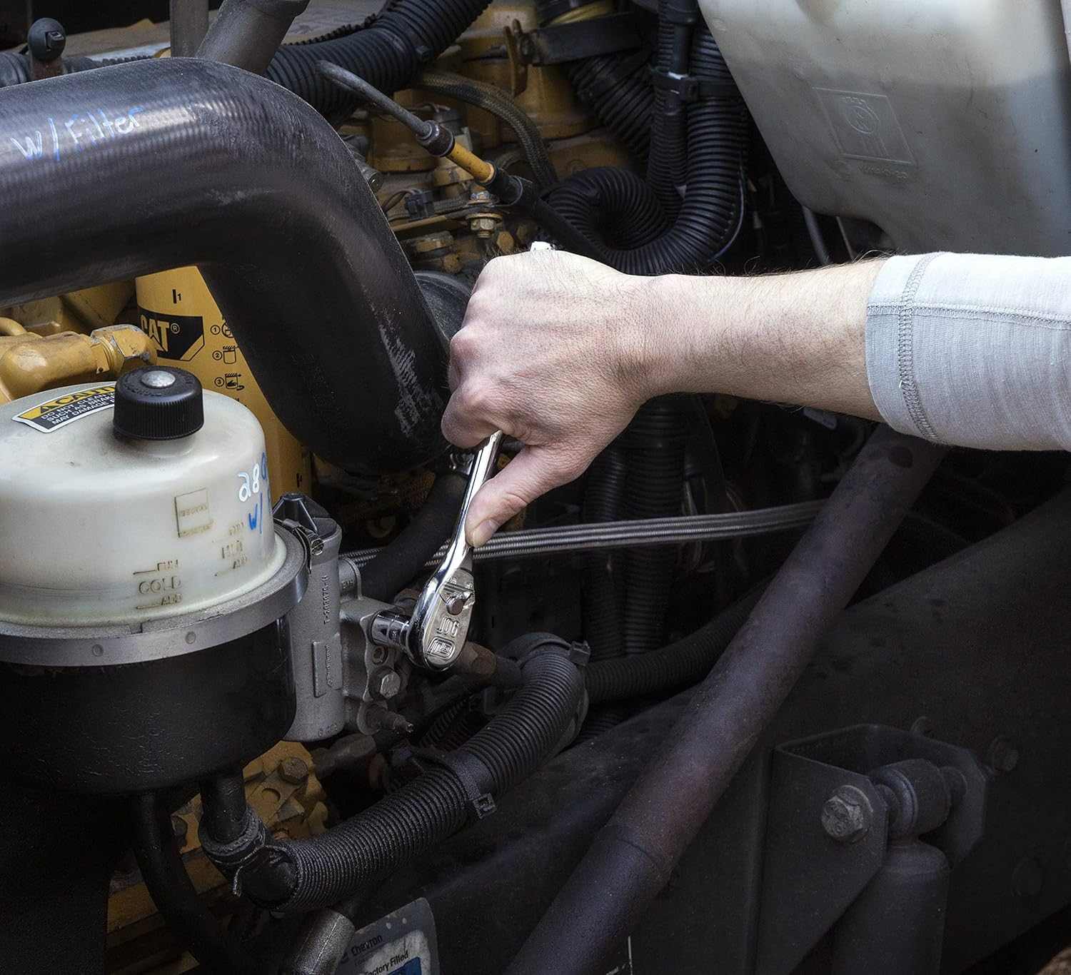 Action shot showing a professional mechanic using a GearWrench 90-tooth ratchet from the 80550 set to perform engine maintenance in a tight vehicle compartment.